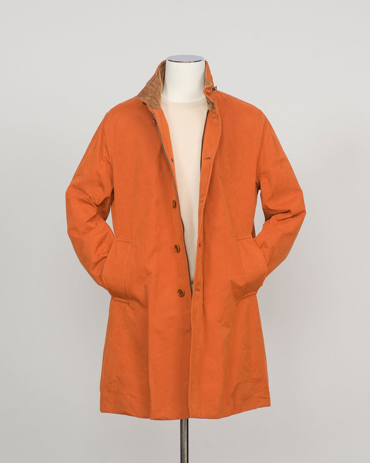 An orange mid-length coat with a brown collar lining, displayed on a white mannequin torso against a light gray background.