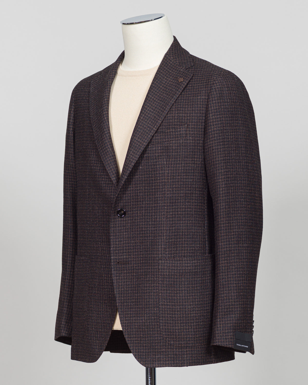 A men's single-breasted blazer in a dark brown and black micro-check pattern, displayed on a white mannequin torso over a light beige shirt, against a neutral gray background. Classic houndstooth sport jacket in rich dark brown. Italian tailoring with refined construction and timeless pattern versatility. Perfect for layering or as a standalone piece for business and weekend wear. Tagliatore Houndstooth Jacket / Dark Brown