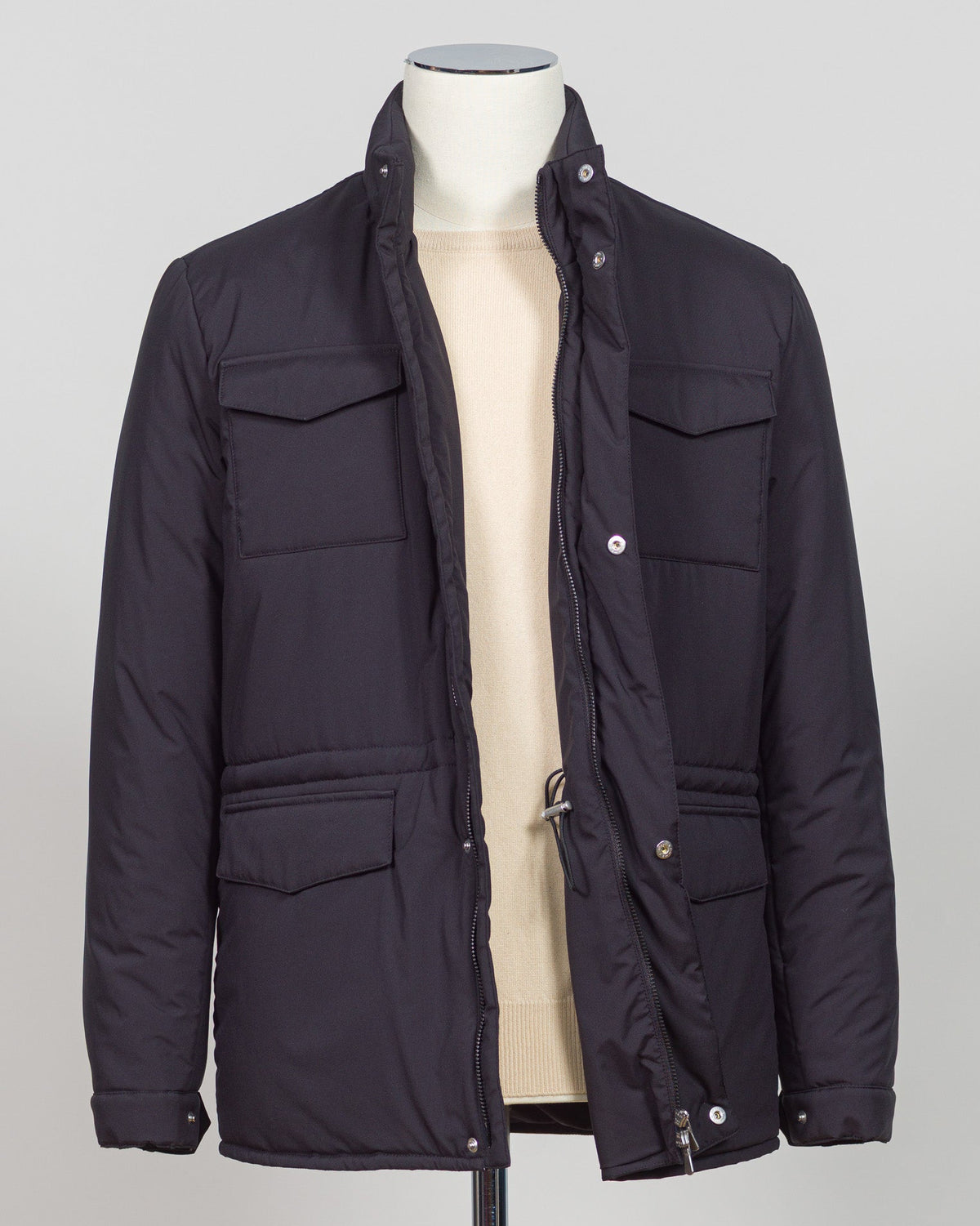 A dark navy blue quilted jacket displayed on a white mannequin torso against a neutral light gray The Gran Sasso Padded Nylon Jacket in navy delivers genuine warmth without the weight. Its lightweight thermowadding construction and refined collar offer understated sophistication—equally at home over a dress shirt or layered with knitwear. Italian craftsmanship meets everyday practicality: polished for client meetings, reliable for daily wear, and versatile enough to become your most trusted layerbackground.