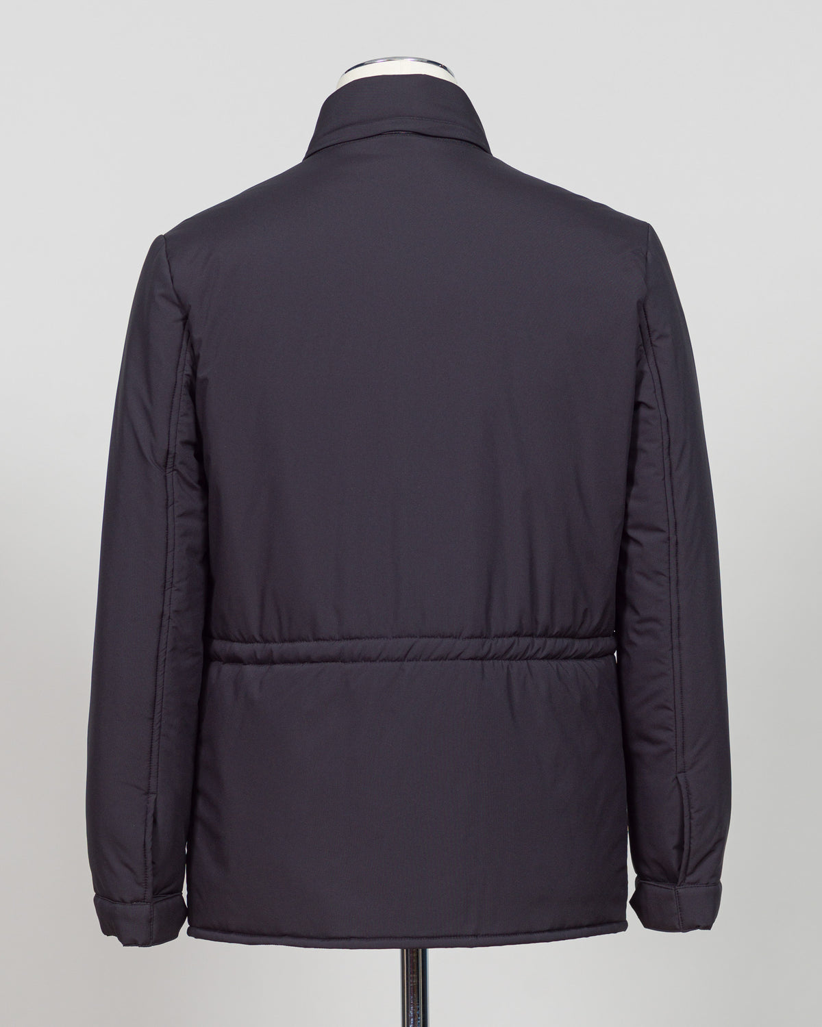 A dark navy blue quilted jacket displayed on a white mannequin torso against a neutral light gray The Gran Sasso Padded Nylon Jacket in navy delivers genuine warmth without the weight. Its lightweight thermowadding construction and refined collar offer understated sophistication—equally at home over a dress shirt or layered with knitwear. Italian craftsmanship meets everyday practicality: polished for client meetings, reliable for daily wear, and versatile enough to become your most trusted layerbackground.