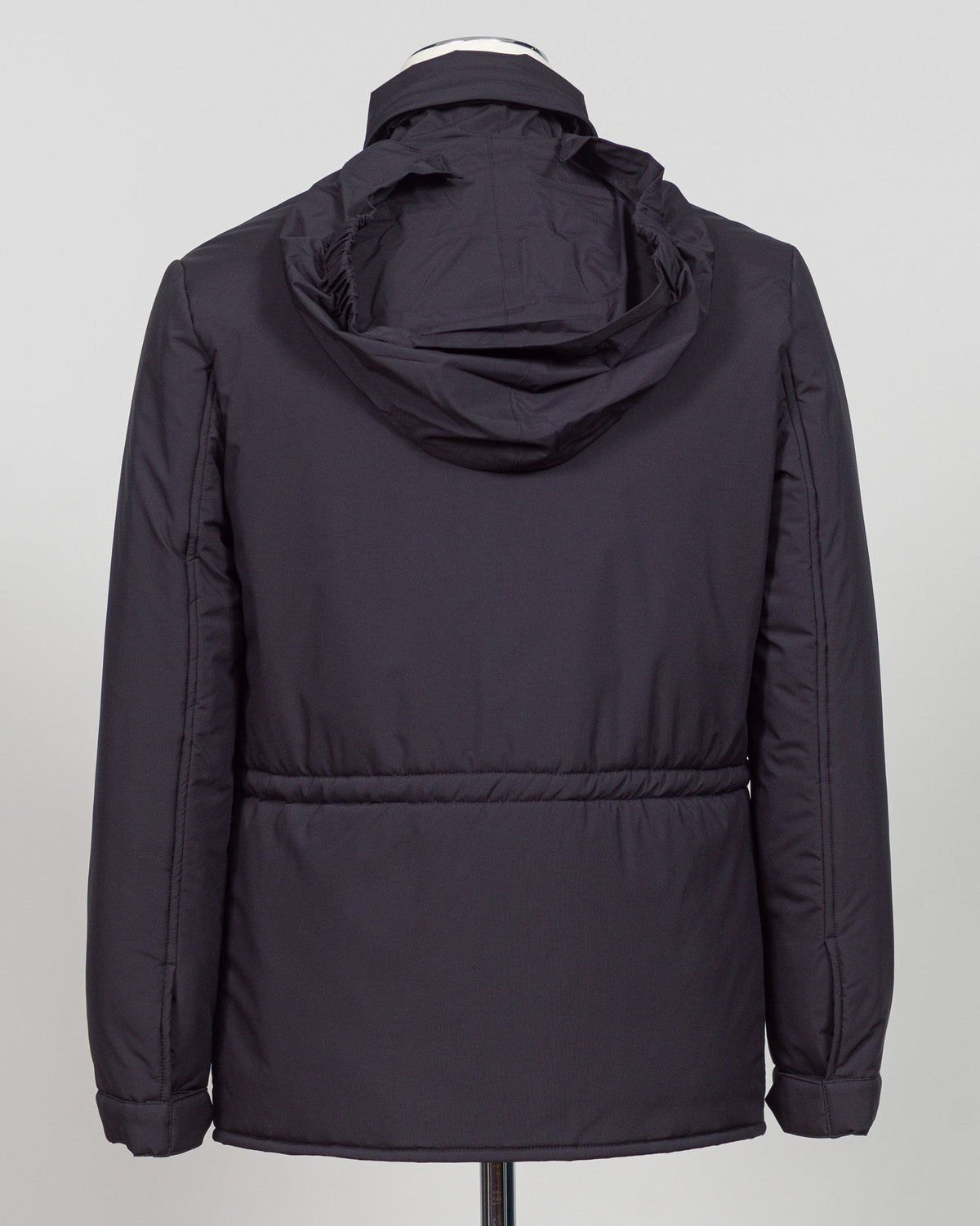A dark navy blue quilted jacket displayed on a white mannequin torso against a neutral light gray The Gran Sasso Padded Nylon Jacket in navy delivers genuine warmth without the weight. Its lightweight thermowadding construction and refined collar offer understated sophistication—equally at home over a dress shirt or layered with knitwear. Italian craftsmanship meets everyday practicality: polished for client meetings, reliable for daily wear, and versatile enough to become your most trusted layerbackground.