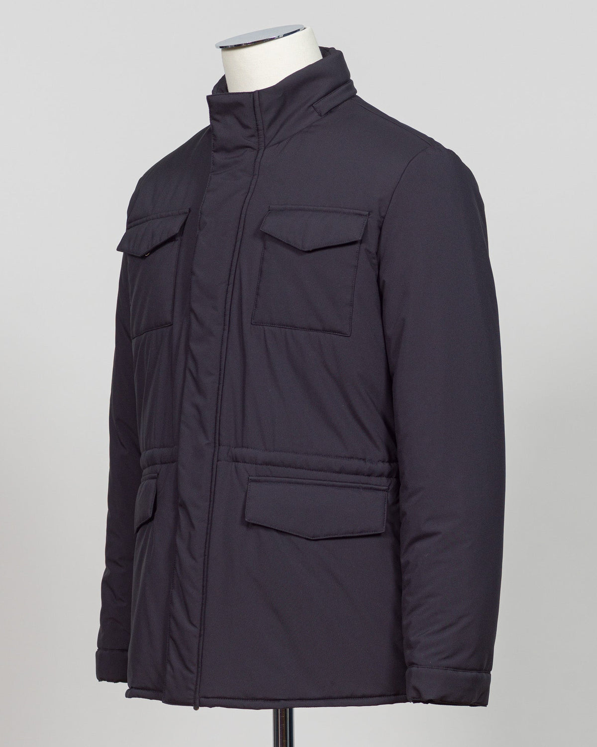 A dark navy blue quilted jacket displayed on a white mannequin torso against a neutral light gray The Gran Sasso Padded Nylon Jacket in navy delivers genuine warmth without the weight. Its lightweight thermowadding construction and refined collar offer understated sophistication—equally at home over a dress shirt or layered with knitwear. Italian craftsmanship meets everyday practicality: polished for client meetings, reliable for daily wear, and versatile enough to become your most trusted layerbackground.