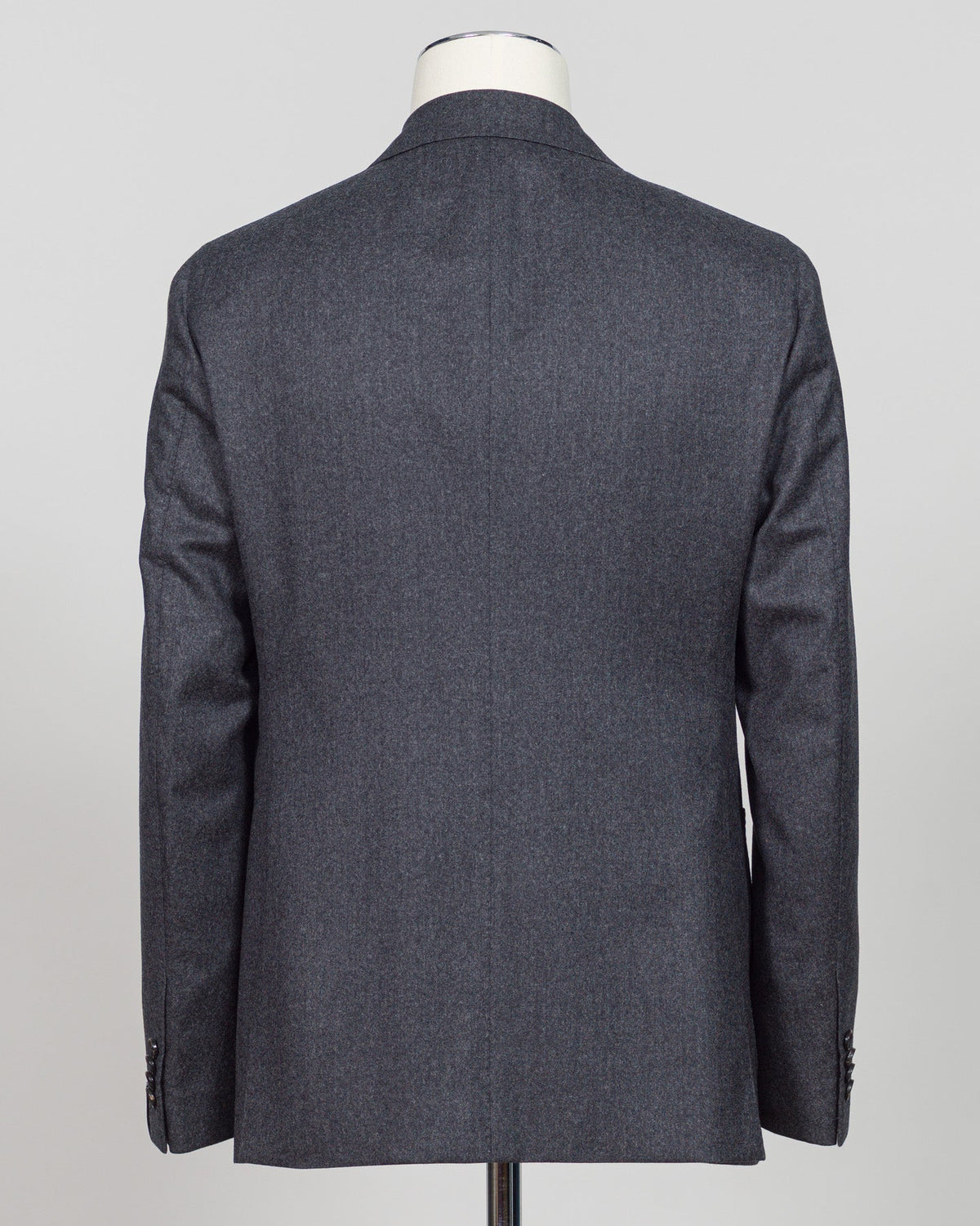 A dark gray textured wool blazer shown from the back on a mannequin torso against a light gray background. Refined elegance in a timeless double-breasted silhouette. This Caruso suit pairs the warmth of quality flannel with sophisticated tailoring, delivering understated luxury suited to both boardroom and evening occasions. Dark grey ensures versatility across your wardrobe while the construction speaks to meticulous craftsmanship and enduring style.Caruso Double-Breasted Flannel Suit / Dark Grey