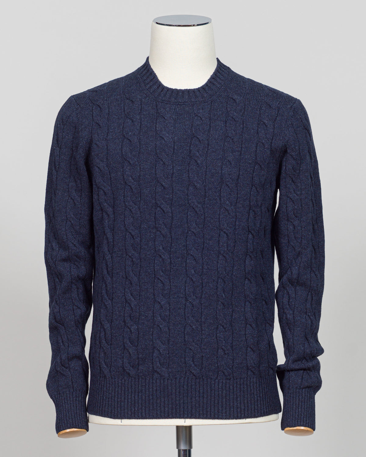 A navy blue cable-knit sweater displayed on a white mannequin torso against a light gray studio background.