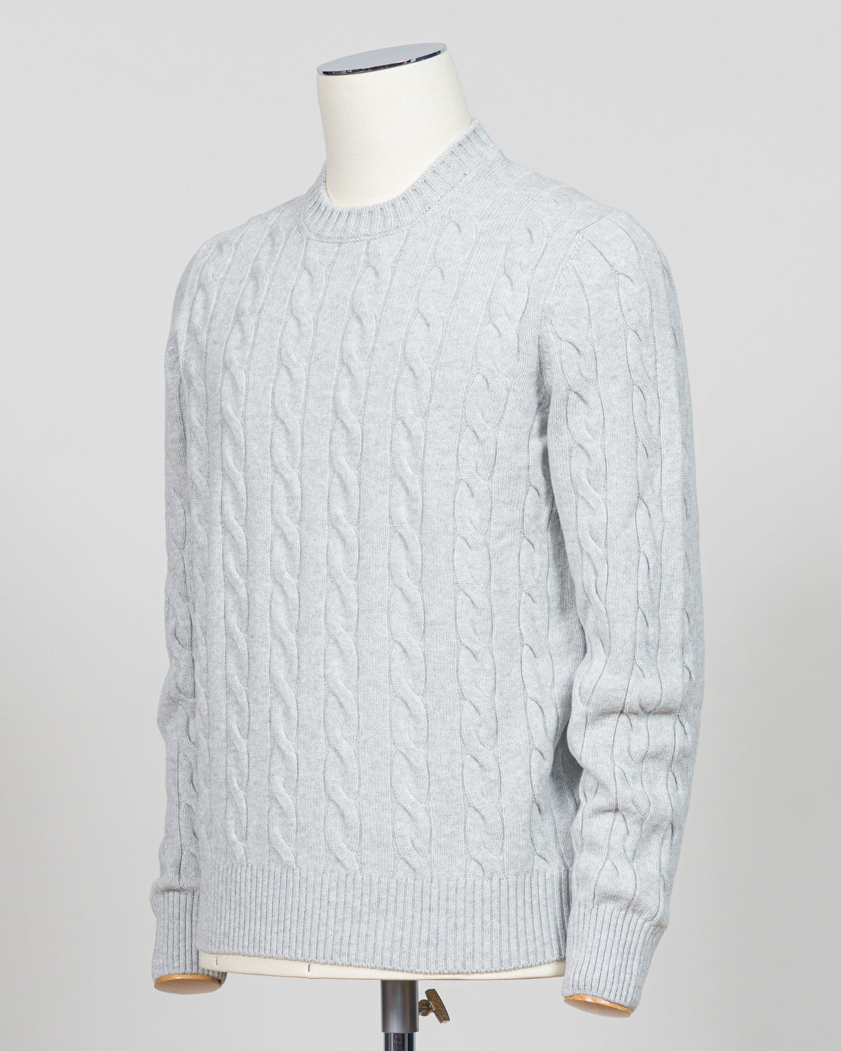 A light gray cable-knit crewneck sweater displayed on a white mannequin torso against a neutral light gray background.