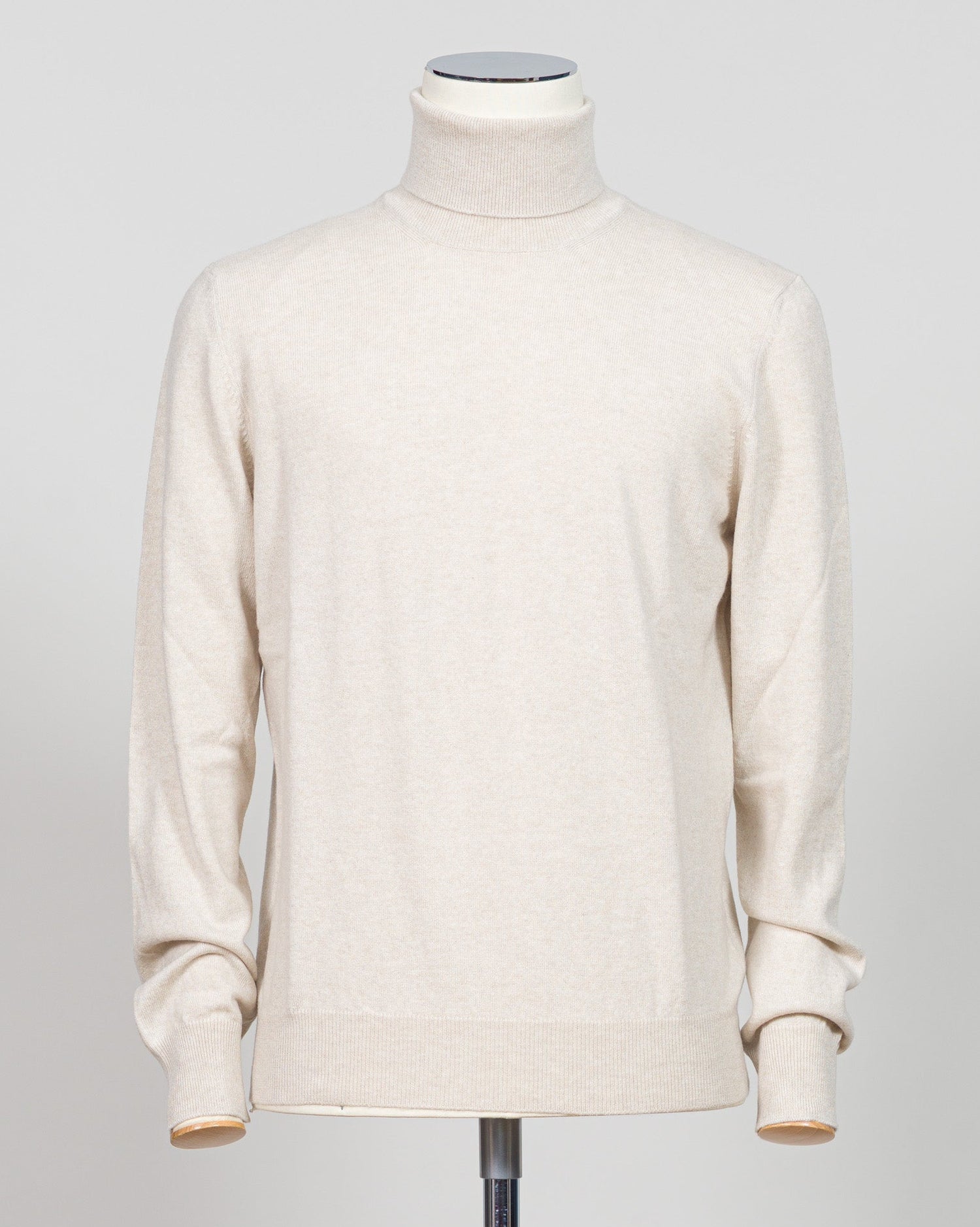 A cream-colored knit turtleneck sweater displayed on a mannequin torso against a light gray studio background. Gran Sasso. Made in Italy.