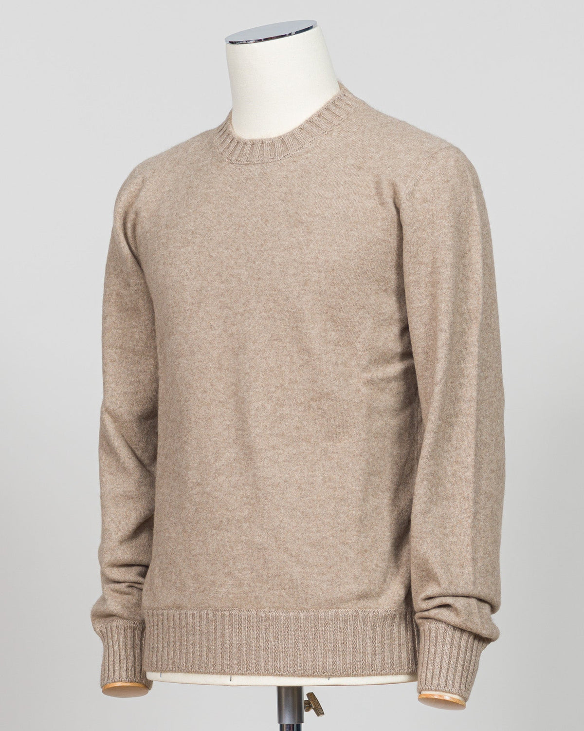 A light beige crewneck knit sweater displayed on a white mannequin torso against a light gray studio background. Italian craftsmanship meets luxurious comfort in this Gran Sasso felted cashmere crewneck. The substantial weight and refined texture of premium cashmere deliver warmth without bulk, while the timeless silver tone pairs effortlessly with tailored trousers or structured outerwear. A foundational piece for the wardrobe—versatile enough for layering, refined enough to stand alone. Gran Sasso