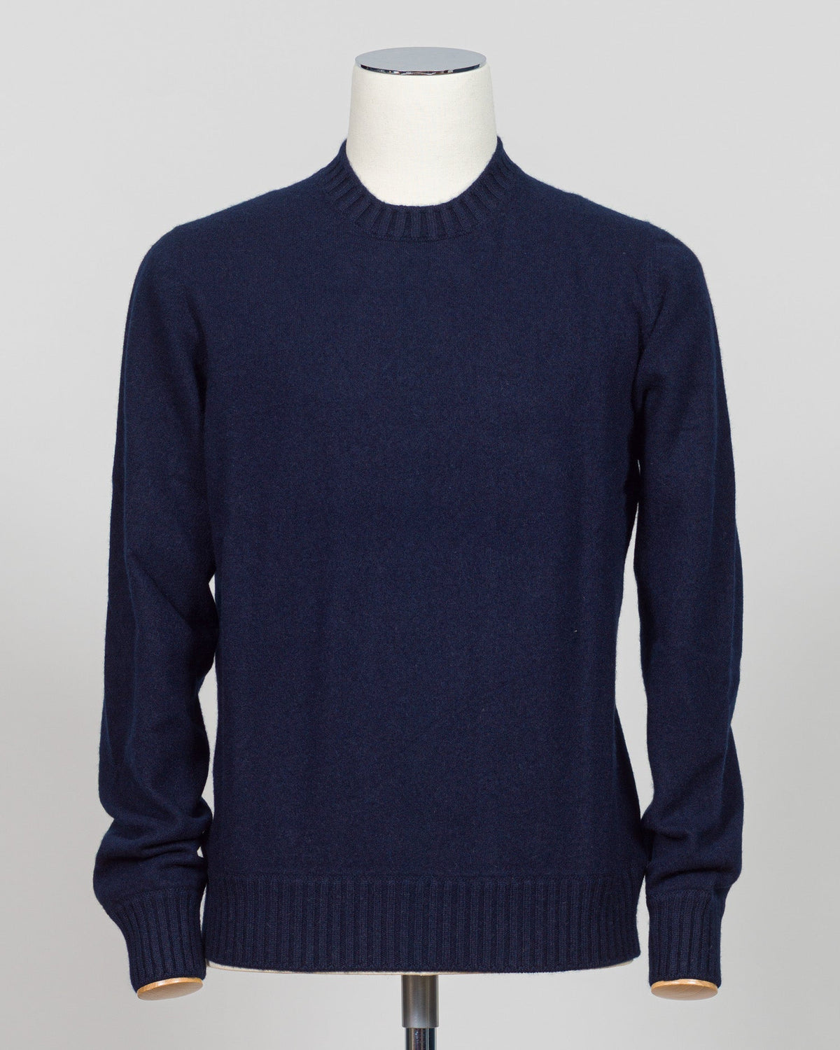 A dark navy blue knit sweater displayed on a white mannequin torso against a light gray studio background. Italian craftsmanship meets luxurious comfort in this Gran Sasso felted cashmere crewneck. The substantial weight and refined texture of premium cashmere deliver warmth without bulk, while the timeless silver tone pairs effortlessly with tailored trousers or structured outerwear. A foundational piece for the wardrobe—versatile enough for layering, refined enough to stand alone. Gran Sasso Felted Cashm