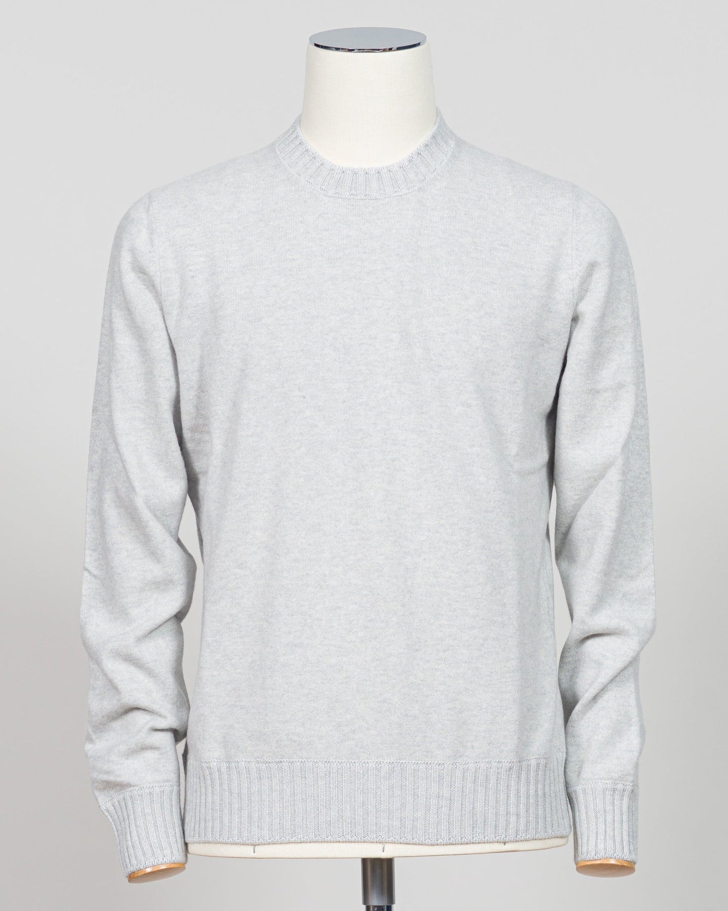 A light gray heathered knit crewneck sweater displayed on a white mannequin torso against a neutral light gray background. Italian craftsmanship meets luxurious comfort in this Gran Sasso felted cashmere crewneck. The substantial weight and refined texture of premium cashmere deliver warmth without bulk, while the timeless silver tone pairs effortlessly with tailored trousers or structured outerwear. A foundational piece for the discerning wardrobe—versatile enough for layering, refined enough to stand alon