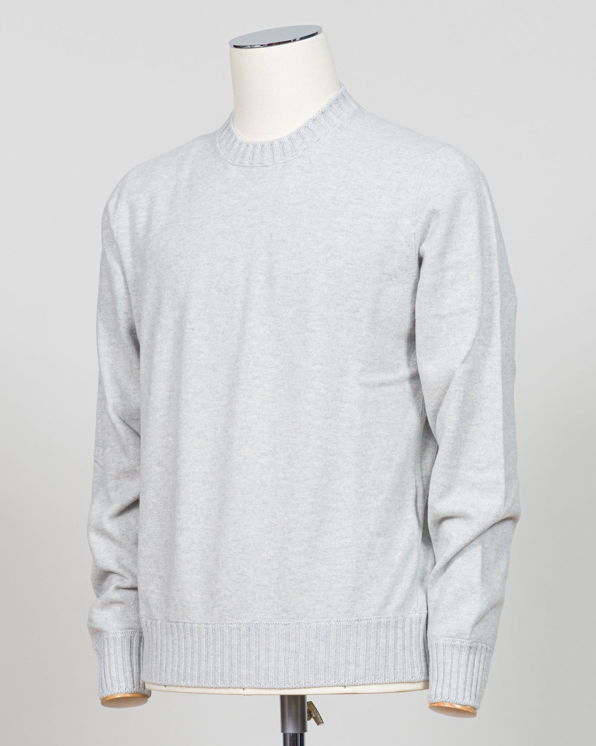 A light gray heather crewneck sweater displayed on a white dress form mannequin against a neutral light gray background. Italian craftsmanship meets luxurious comfort in this Gran Sasso felted cashmere crewneck. The substantial weight and refined texture of premium cashmere deliver warmth without bulk, while the timeless silver tone pairs effortlessly with tailored trousers or structured outerwear. A foundational piece for the discerning wardrobe—versatile enough for layering, refined enough to stand alone.