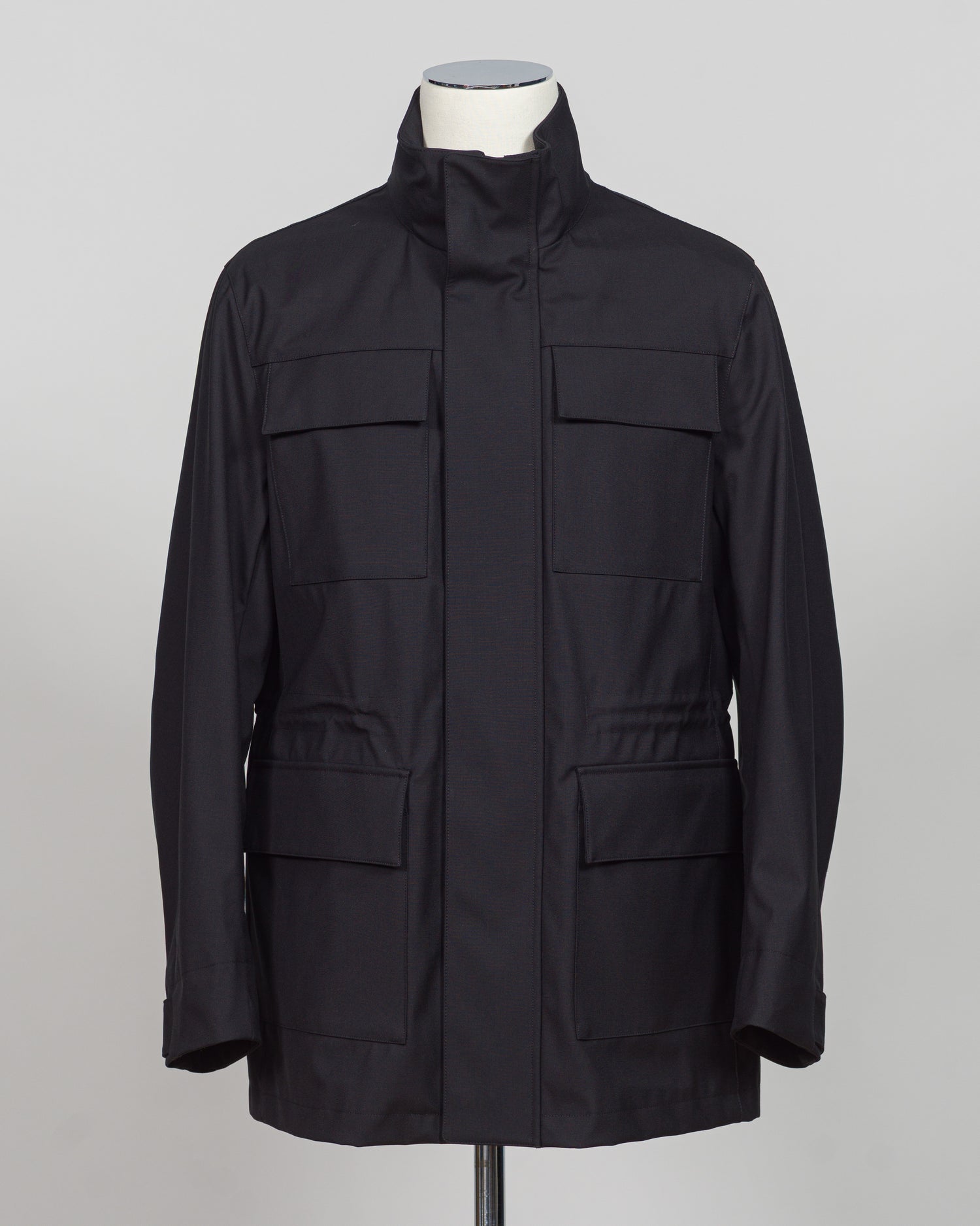 A black utility jacket with a high stand-up collar, displayed on a white mannequin torso against a neutral gray background.