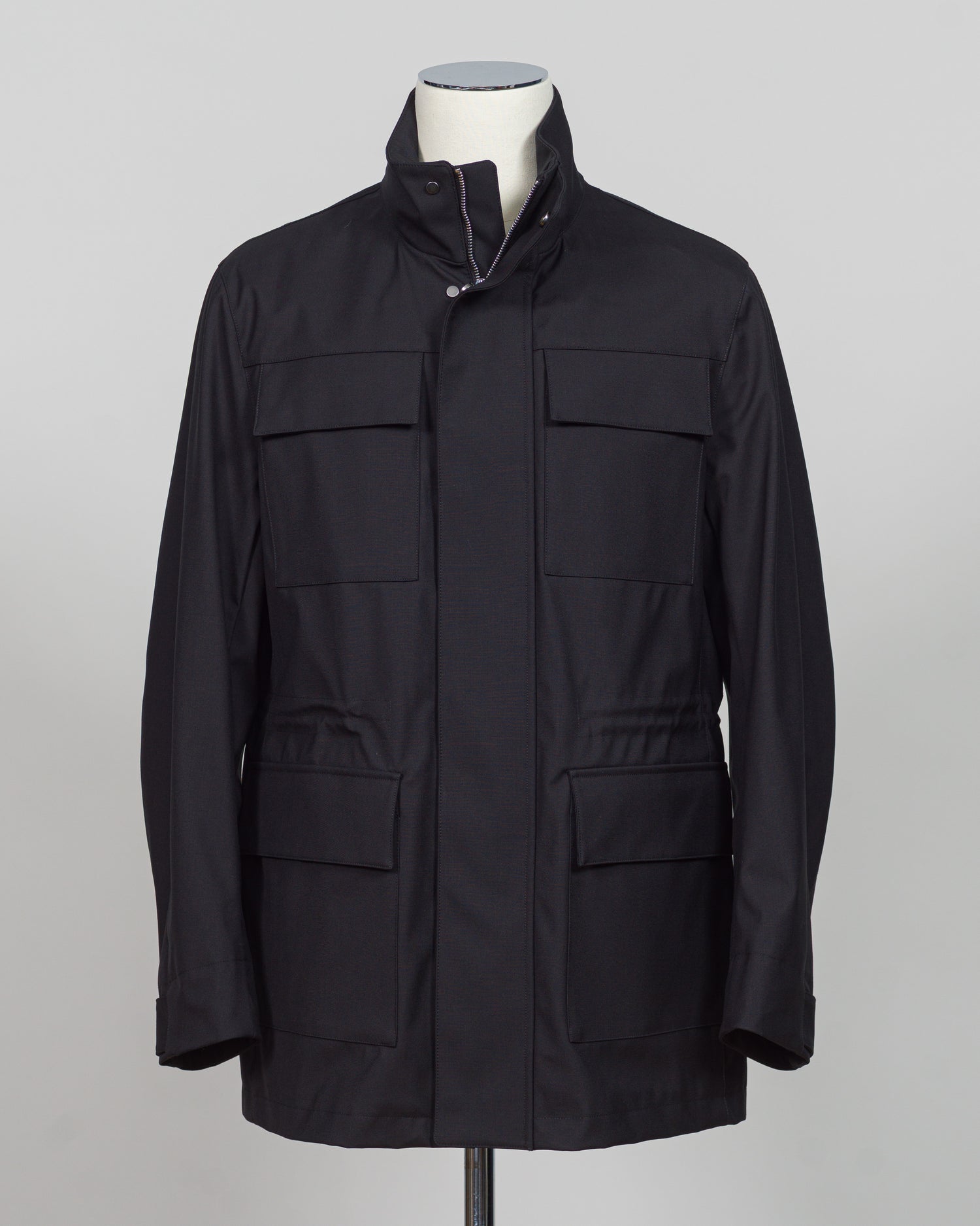 A black utility jacket displayed on a mannequin torso against a light gray studio background. The jacket features a high collar, a front zipper closure, and four large front flap pockets.