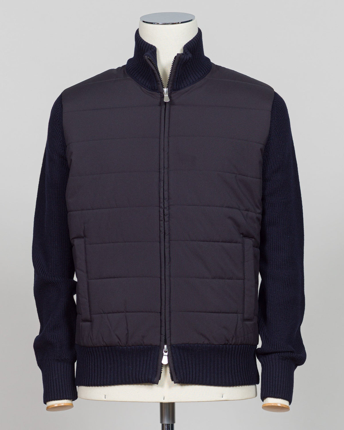 A dark navy blue jacket with a quilted body and ribbed knit sleeves, collar, and hem, displayed on a mannequin against a light gray background. talian wool craftsmanship meets contemporary tailoring in this Gran Sasso sartorial padded jacket. Structured in premium wool with subtle padding for refined warmth, it pairs effortlessly with business wear or elevated casual styling. Gran Sasso Sartorial Padded Wool Jacket / Navy