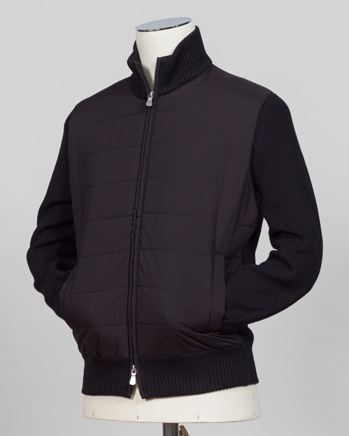 A black zip-up jacket with a quilted front panel and ribbed knit sleeves, collar, and hem, displayed on a mannequin torso against a light gray background. Italian wool craftsmanship meets contemporary tailoring in this Gran Sasso sartorial padded jacket. Structured in premium wool with subtle padding for refined warmth, it pairs effortlessly with business wear or elevated casual styling. Gran Sasso Sartorial Padded Wool Jacket / Black