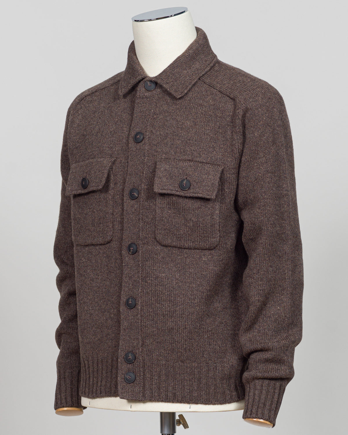 A brown knit button-front cardigan sweater displayed on a mannequin torso against a light gray studio background. The cardigan has a collar, long sleeves, ribbed cuffs and hem, and two large chest flap pockets with dark buttons.