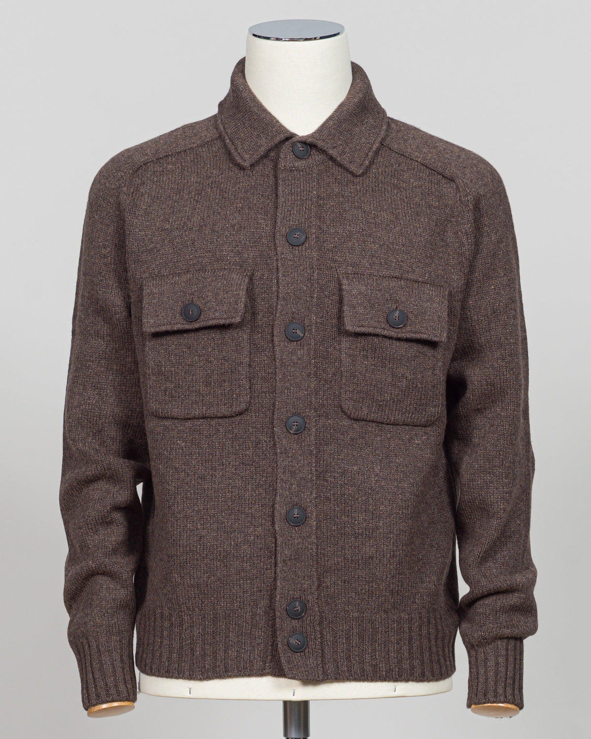 A brown knit button-front cardigan sweater with a pointed collar and two flap chest pockets, displayed on a mannequin torso against a light gray studio background.