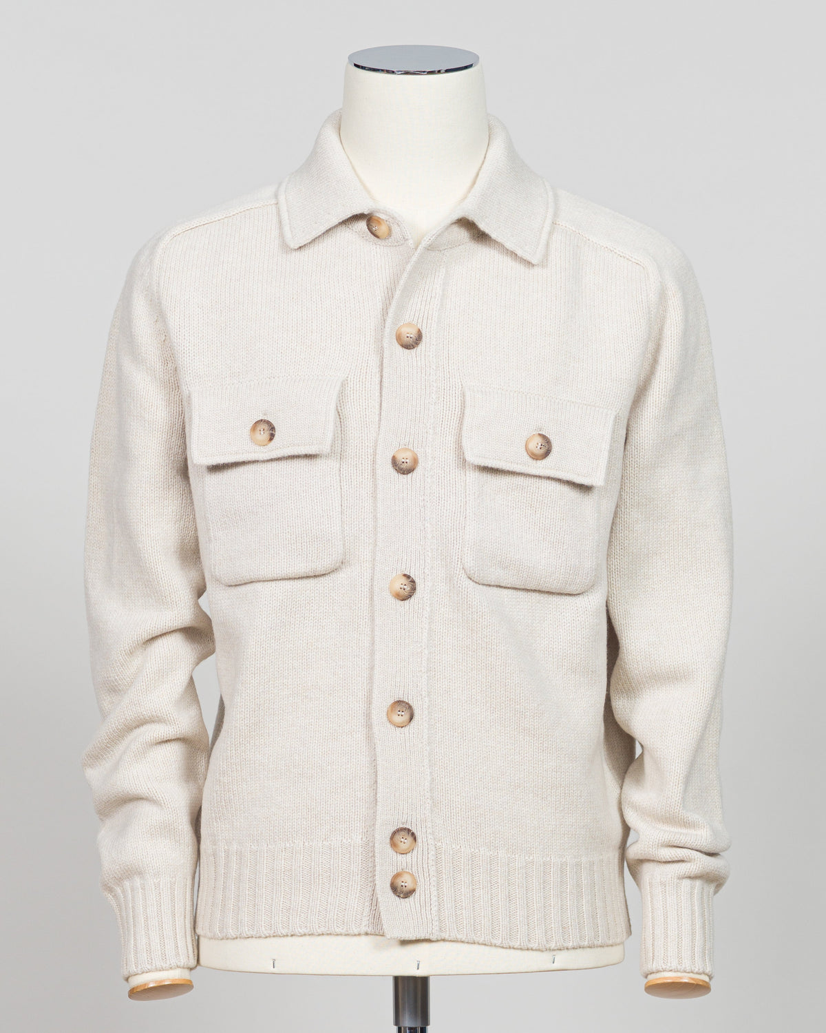 An off-white knit cardigan sweater with brown buttons, displayed on a cream-colored mannequin against a light gray background.