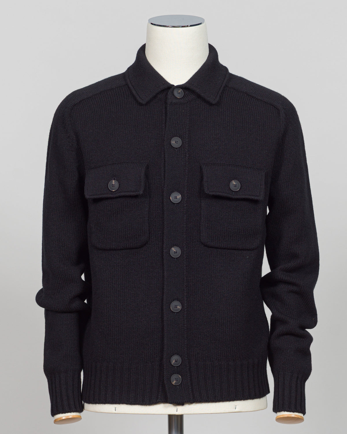 A black knit button-up cardigan sweater with a collar and two chest flap pockets, displayed on a mannequin torso against a light gray background.