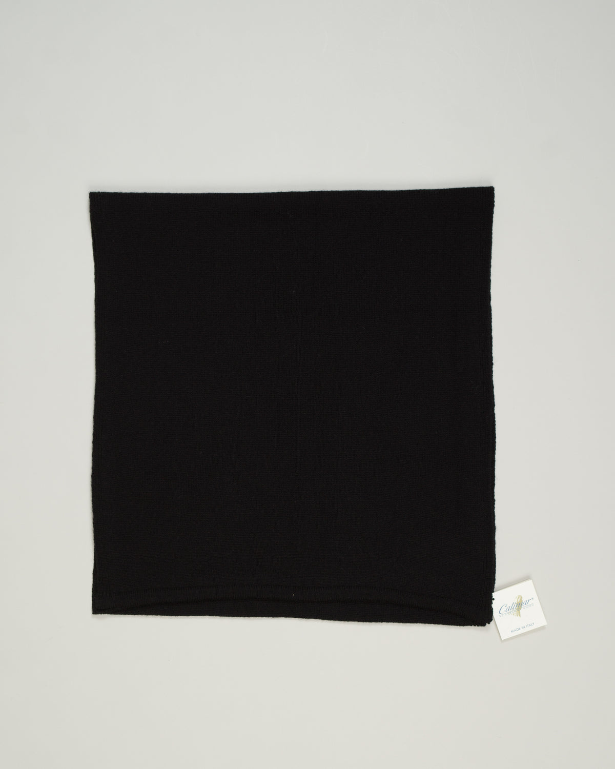 A black knit neck warmer or balaclava laid flat on a light gray background, with a small white brand tag visible at the bottom right corner.