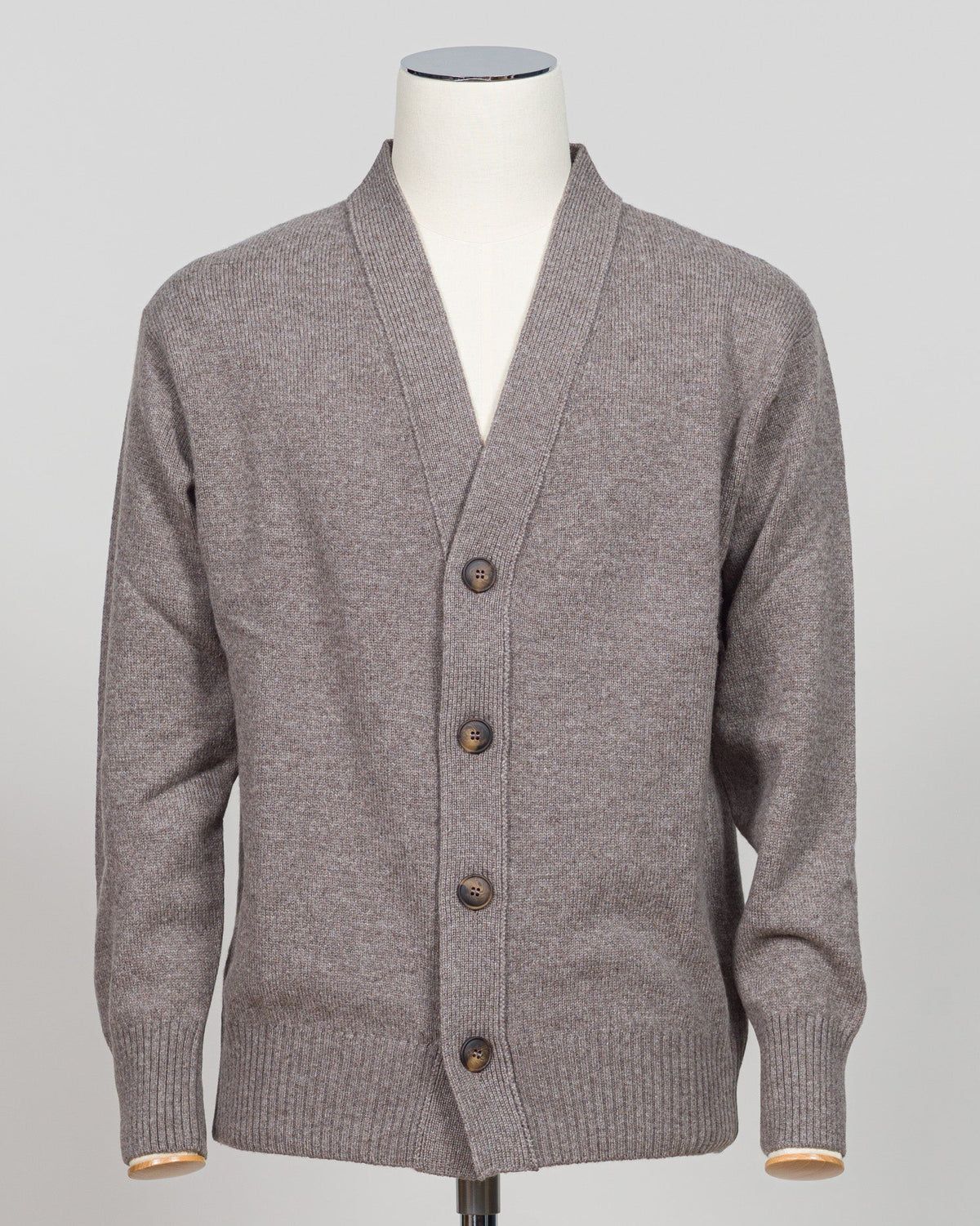 A gray knit cardigan sweater displayed on a white mannequin torso against a light gray studio background. The cardigan has a V-neck, front button closure with dark brown buttons, ribbed cuffs, and ribbed hem. Gran Sasso's timeless cashmere crew neck in soft beige epitomizes understated luxury. Crafted from 100% pure cashmere with a vintage-washed finish that develops character with wear, this Italian-made essential features a relaxed fashion fit, ribbed detailing at the hem and cuffs, and a refined crew ne