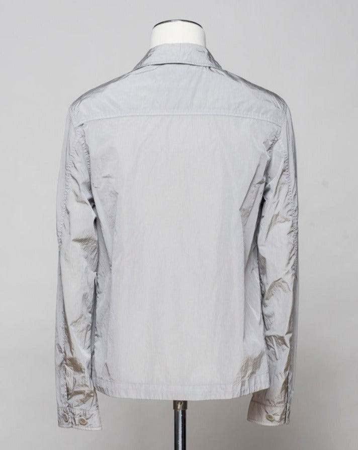 Button fastening in front. 2 breast pockets with buttons. Small pocket on left arm with snap fastener. Embroidered tone-on-tone C.P. Company logo on left pocket. Article: 16CMOS106A 005904G. Composition: 100% pre-consumer recycled nylon. Garment dyed. Color: 913 / Drizzle Grey