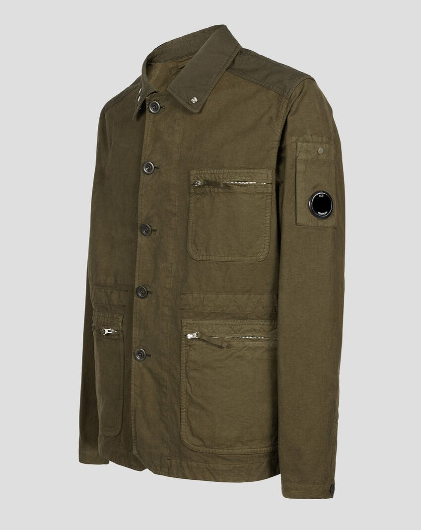 Classic collar Button storm flap Lens detail Secure zip compartments Adjustable waist and cuffs Garment dyed Article: 14CMOW245A 006354G Color: Ivy Green / 683 Composition: 100% Cotton Chore jacket in Mais B, the contemporary version of the first Mais fabric, one of the foundation fabrics at the birth of C.P. Company. A broadcloth weave variation of the traditional English two tone gabardines used for raincoats, it is especially suitable for summer outerwear with a workwear aesthetic.