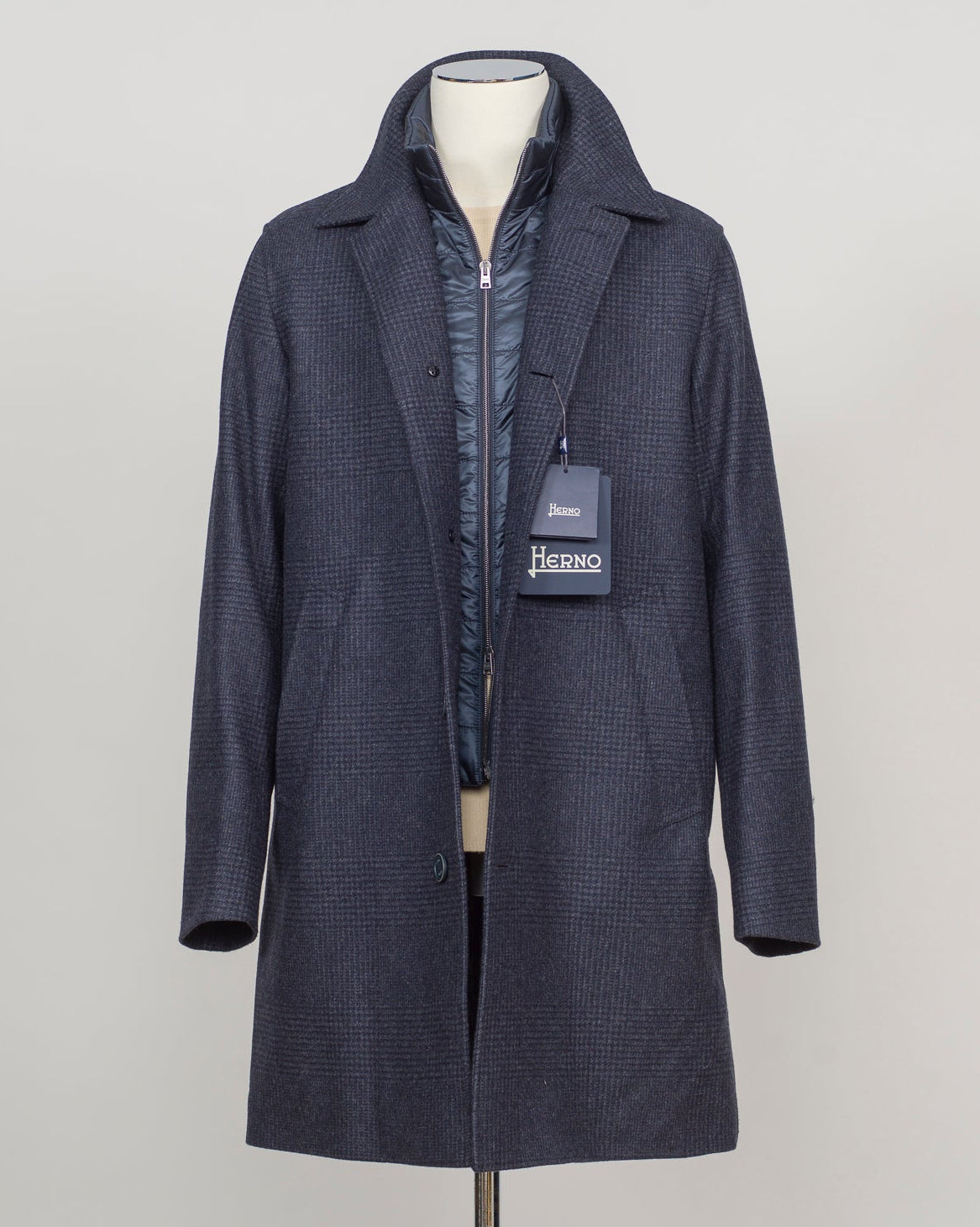 Iconic Herno wool coat in refined glencheck, balancing navy and blue for understated luxury. Fully lined for structured layering across seasons. Features a detachable bib for versatile styling—wear it integrated for classic formality or remove for a streamlined silhouette. Italian craftsmanship and meticulous tailoring define this essential investment piece. Herno Lined Glencheck Wool Coat / Navy & Blue