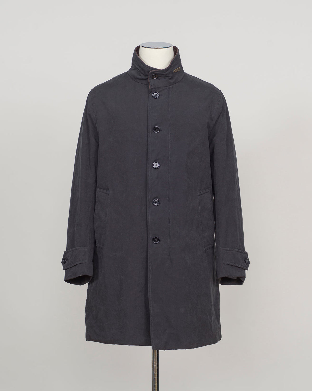 A dark charcoal gray mid-length coat with a high stand collar and front buttons, displayed on a mannequin torso against a light gray studio background.