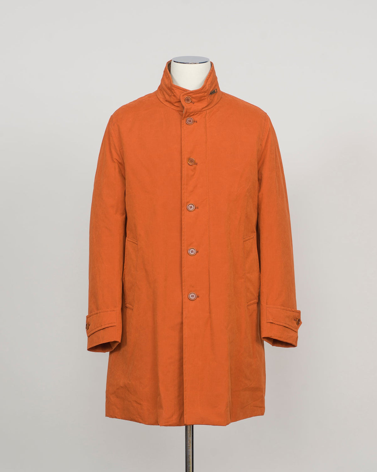 An orange mid-length coat with a stand collar and front buttons, displayed on a mannequin torso against a light gray background.
