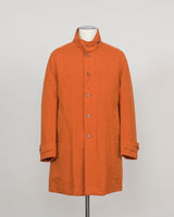 An orange mid-length coat with a stand collar and front buttons, displayed on a mannequin torso against a light gray background.
