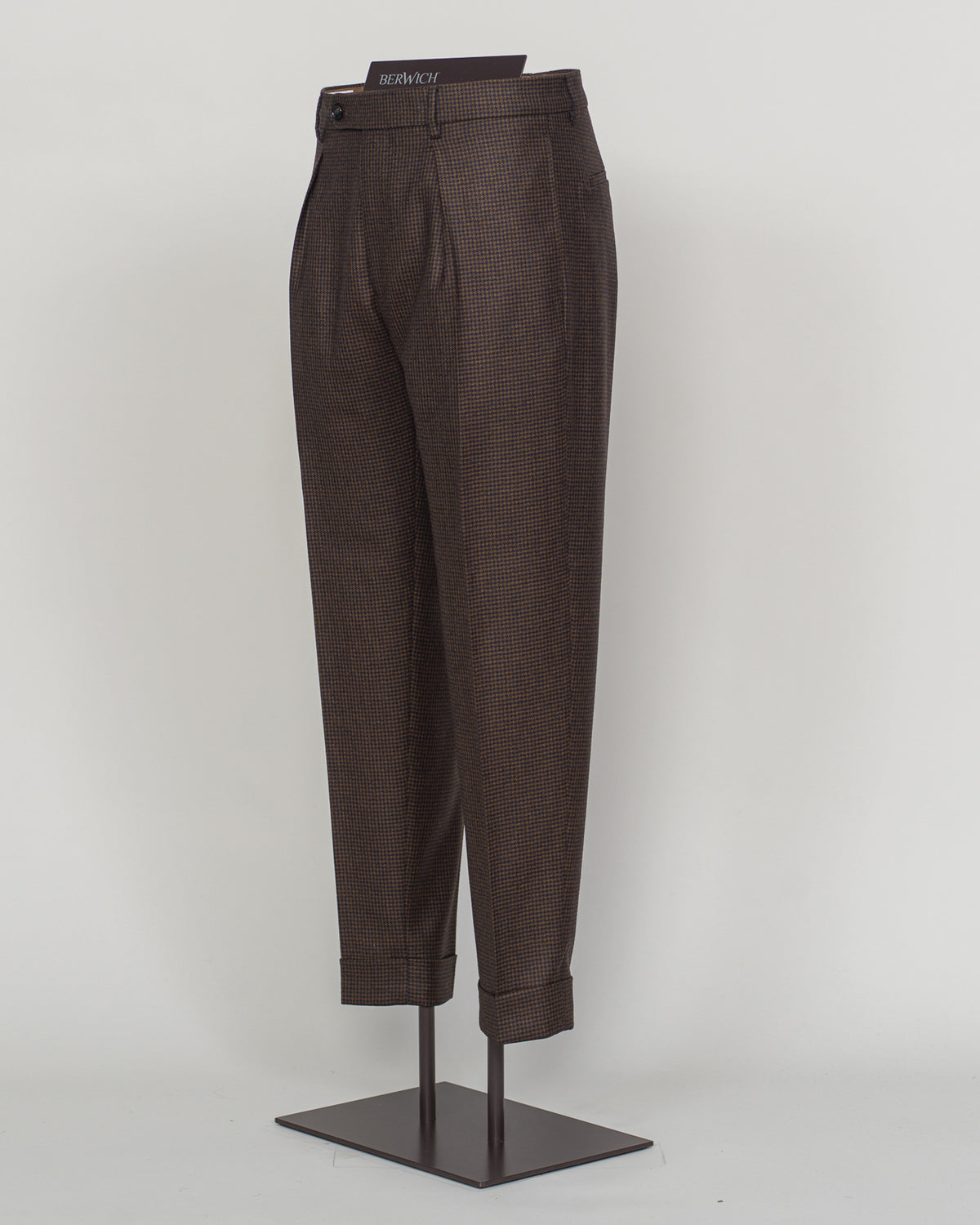 Berwich's Chiaia trousers showcase Italian tailoring heritage with a refined puppytooth pattern in brown. Cut with a contemporary silhouette and finished with precision pleating, these trousers balance classic structure with modern sophistication. The carefully selected fabric drapes with quiet elegance, making them an essential foundation for curated menswear wardrobes that demand both substance and understated style.