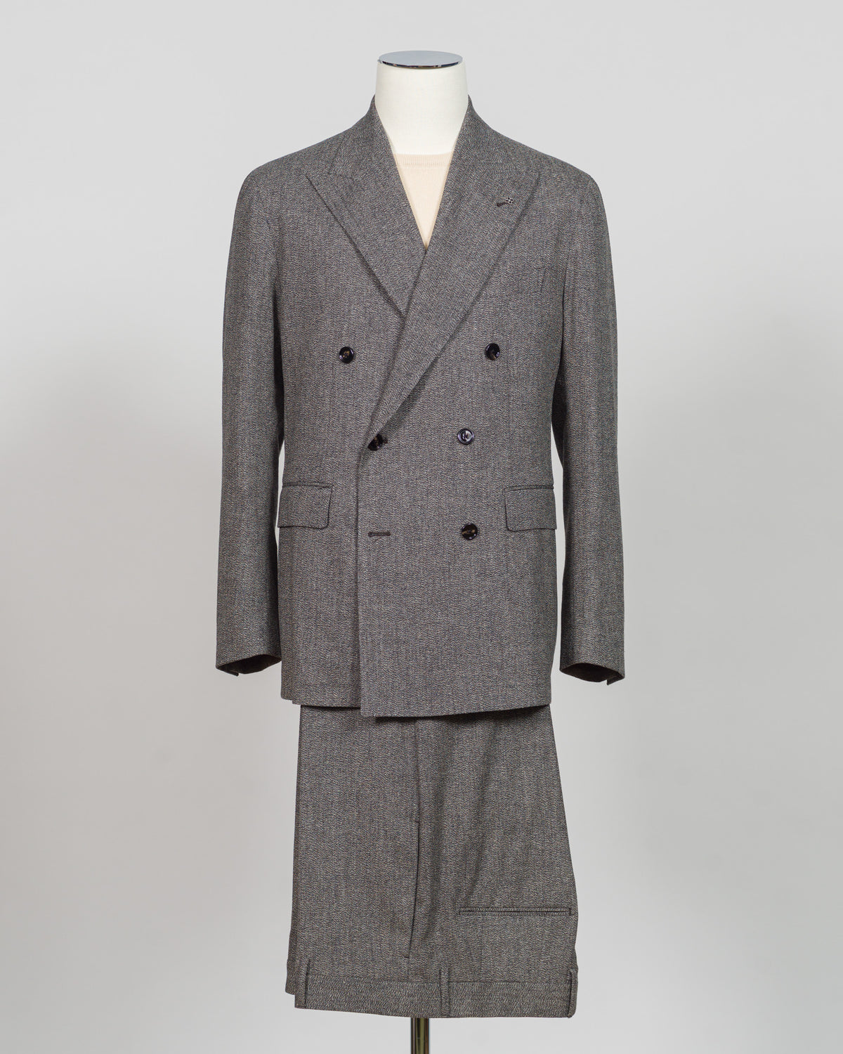 A gray double-breasted suit with a matching skirt, displayed on a mannequin against a light gray background. Tagliatore's double-breasted silhouette merges Italian craftsmanship with refined restraint. The brown and grey palette offers versatility across seasons and occasions—from boardroom formality to sophisticated evening wear. Carefully finished details and structured shoulders create a commanding presence while maintaining contemporary proportion. Cut for the discerning wearer who values timeless tailo