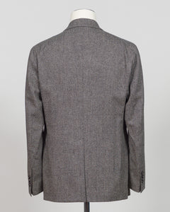 The back view of a men's gray herringbone tweed blazer displayed on a white mannequin torso against a light gray background. Tagliatore's double-breasted silhouette merges Italian craftsmanship with refined restraint. The brown and grey palette offers versatility across seasons and occasions—from boardroom formality to sophisticated evening wear. Carefully finished details and structured shoulders create a commanding presence while maintaining contemporary proportion. Cut for the discerning wearer who value