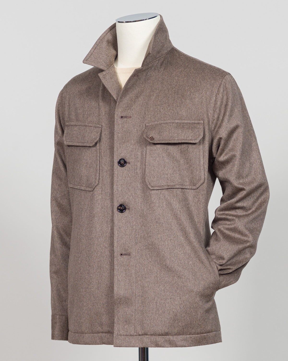 A brown textured wool overshirt jacket with a high collar, three-quarter button closure, and two large chest flap pockets, displayed on a mannequin torso against a light gray background. Luxurious overshirt crafted from a cashmere and wool blend in a sophisticated taupe tone. The Tagliatore piece delivers refined layering with a substantial drape and premium hand-feel. Perfect for elevated casual wear or as a versatile shirt jacket that transitions effortlessly through seasons. Italian tailoring meets every