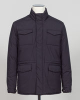 A dark navy blue quilted jacket displayed on a white mannequin torso against a neutral light gray The Gran Sasso Padded Nylon Jacket in navy delivers genuine warmth without the weight. Its lightweight thermowadding construction and refined collar offer understated sophistication—equally at home over a dress shirt or layered with knitwear. Italian craftsmanship meets everyday practicality: polished for client meetings, reliable for daily wear, and versatile enough to become your most trusted layerbackground.