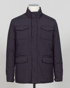 A dark navy blue quilted jacket displayed on a white mannequin torso against a neutral light gray The Gran Sasso Padded Nylon Jacket in navy delivers genuine warmth without the weight. Its lightweight thermowadding construction and refined collar offer understated sophistication—equally at home over a dress shirt or layered with knitwear. Italian craftsmanship meets everyday practicality: polished for client meetings, reliable for daily wear, and versatile enough to become your most trusted layerbackground.