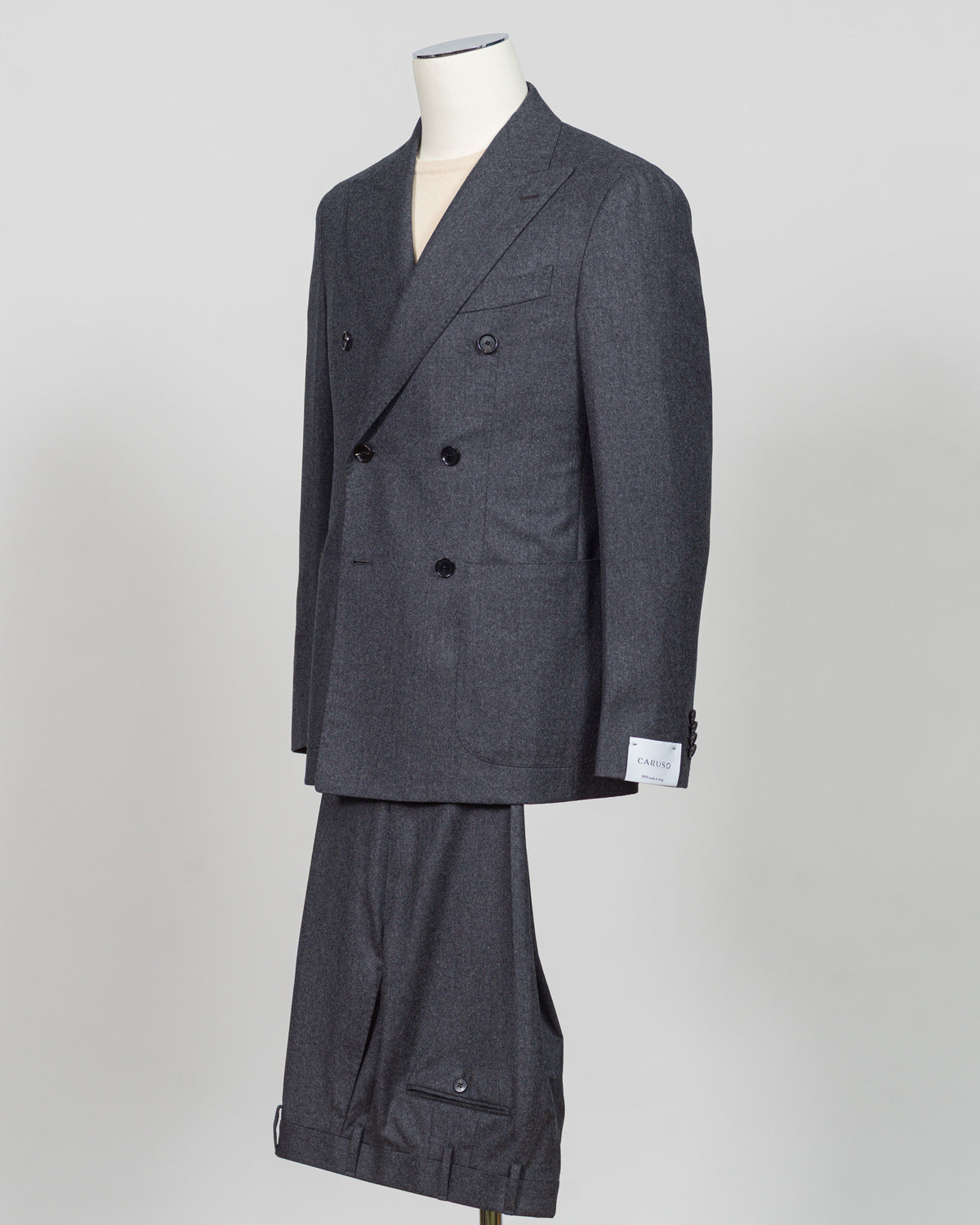 A dark gray double-breasted suit with a subtle micro-houndstooth pattern, displayed on a mannequin against a light gray background. Refined elegance in a timeless double-breasted silhouette. This Caruso suit pairs the warmth of quality flannel with sophisticated tailoring, delivering understated luxury suited to both boardroom and evening occasions. Dark grey ensures versatility across your wardrobe while the construction speaks to meticulous craftsmanship and enduring style.Caruso Double-Breasted Flannel S