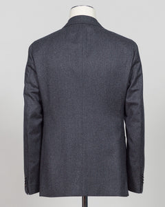 A dark gray textured wool blazer shown from the back on a mannequin torso against a light gray background. Refined elegance in a timeless double-breasted silhouette. This Caruso suit pairs the warmth of quality flannel with sophisticated tailoring, delivering understated luxury suited to both boardroom and evening occasions. Dark grey ensures versatility across your wardrobe while the construction speaks to meticulous craftsmanship and enduring style.Caruso Double-Breasted Flannel Suit / Dark Grey
