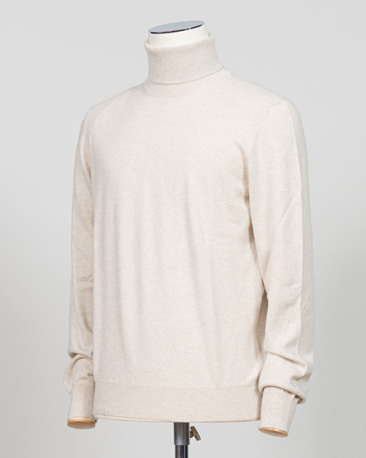 A cream-colored knit turtleneck sweater displayed on a mannequin torso against a light gray studio background. Gran Sasso. Made in Italy.
