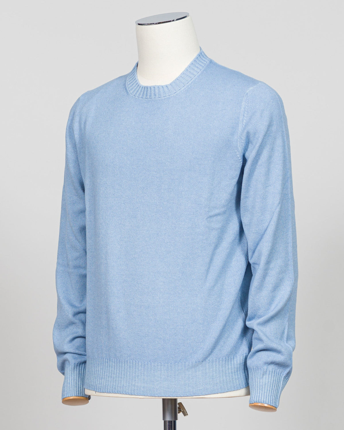 A light blue crewneck sweater displayed on a white mannequin torso against a light gray studio background. Italian luxury knitwear in a soft light blue. Gran Sasso's refined crewneck delivers timeless sophistication with superior craftsmanship—a versatile layering piece that pairs effortlessly with tailored trousers or casual separates. Premium construction ensures lasting comfort and durability. Gran Sasso Vintage Crewneck / Light Blue
