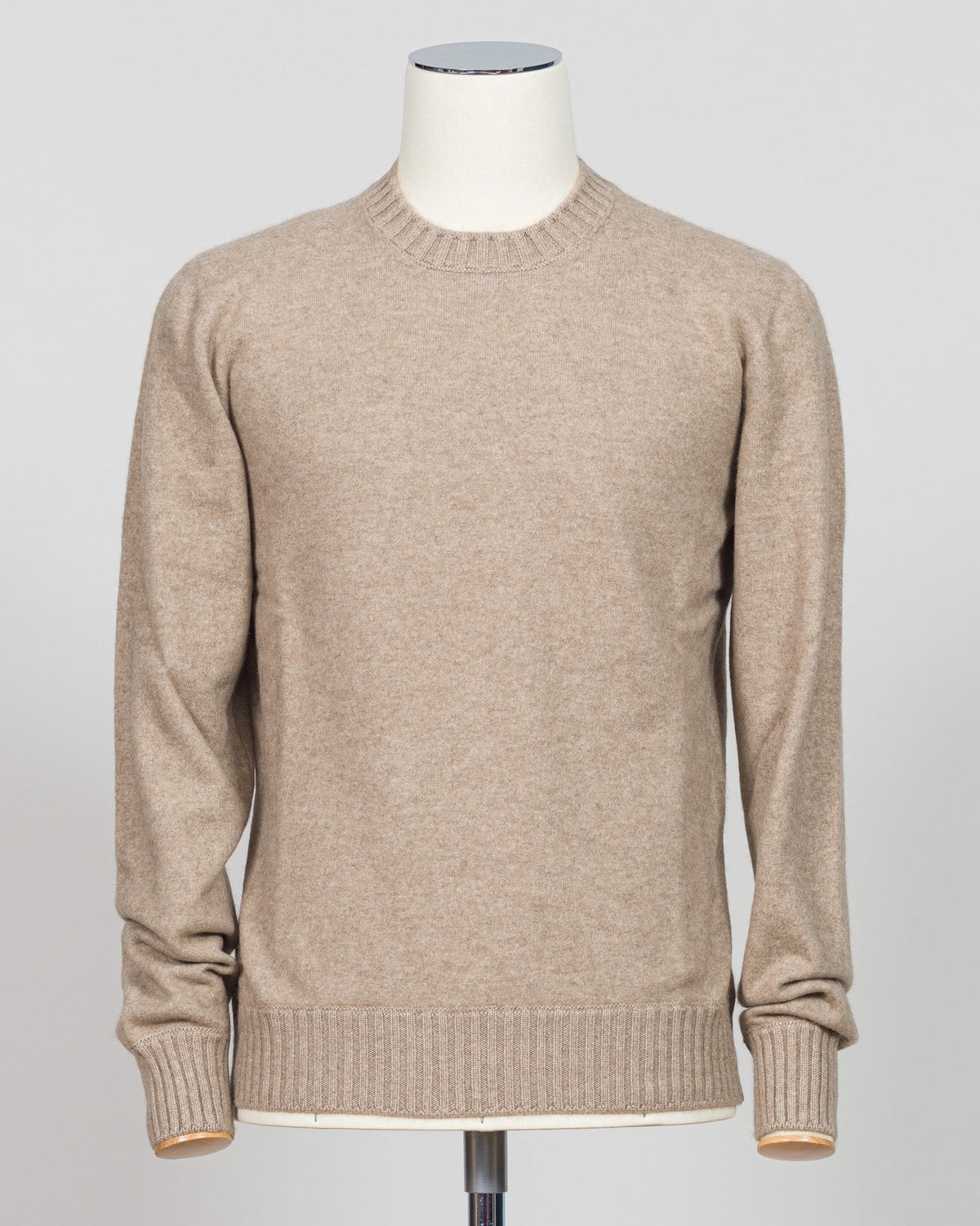 A light beige crewneck knit sweater displayed on a white mannequin torso against a light gray studio background. Italian craftsmanship meets luxurious comfort in this Gran Sasso felted cashmere crewneck. The substantial weight and refined texture of premium cashmere deliver warmth without bulk, while the timeless silver tone pairs effortlessly with tailored trousers or structured outerwear. A foundational piece for the wardrobe—versatile enough for layering, refined enough to stand alone. Gran Sasso