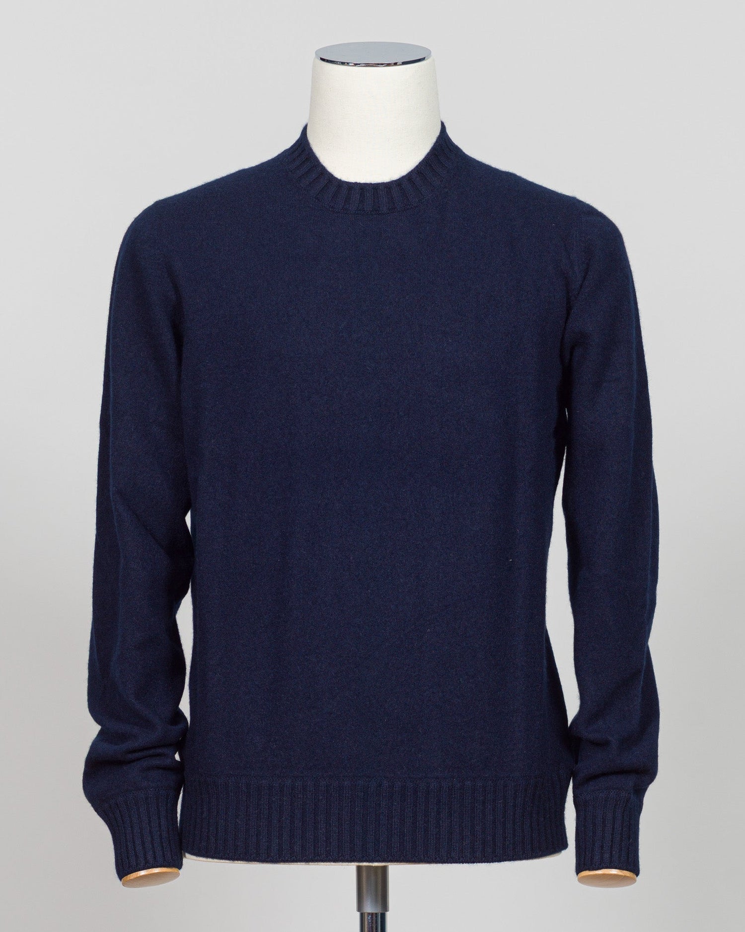 A dark navy blue knit sweater displayed on a white mannequin torso against a light gray studio background. Italian craftsmanship meets luxurious comfort in this Gran Sasso felted cashmere crewneck. The substantial weight and refined texture of premium cashmere deliver warmth without bulk, while the timeless silver tone pairs effortlessly with tailored trousers or structured outerwear.  A foundational piece for the wardrobe—versatile enough for layering, refined enough to stand alone. Gran Sasso Felted Cashm