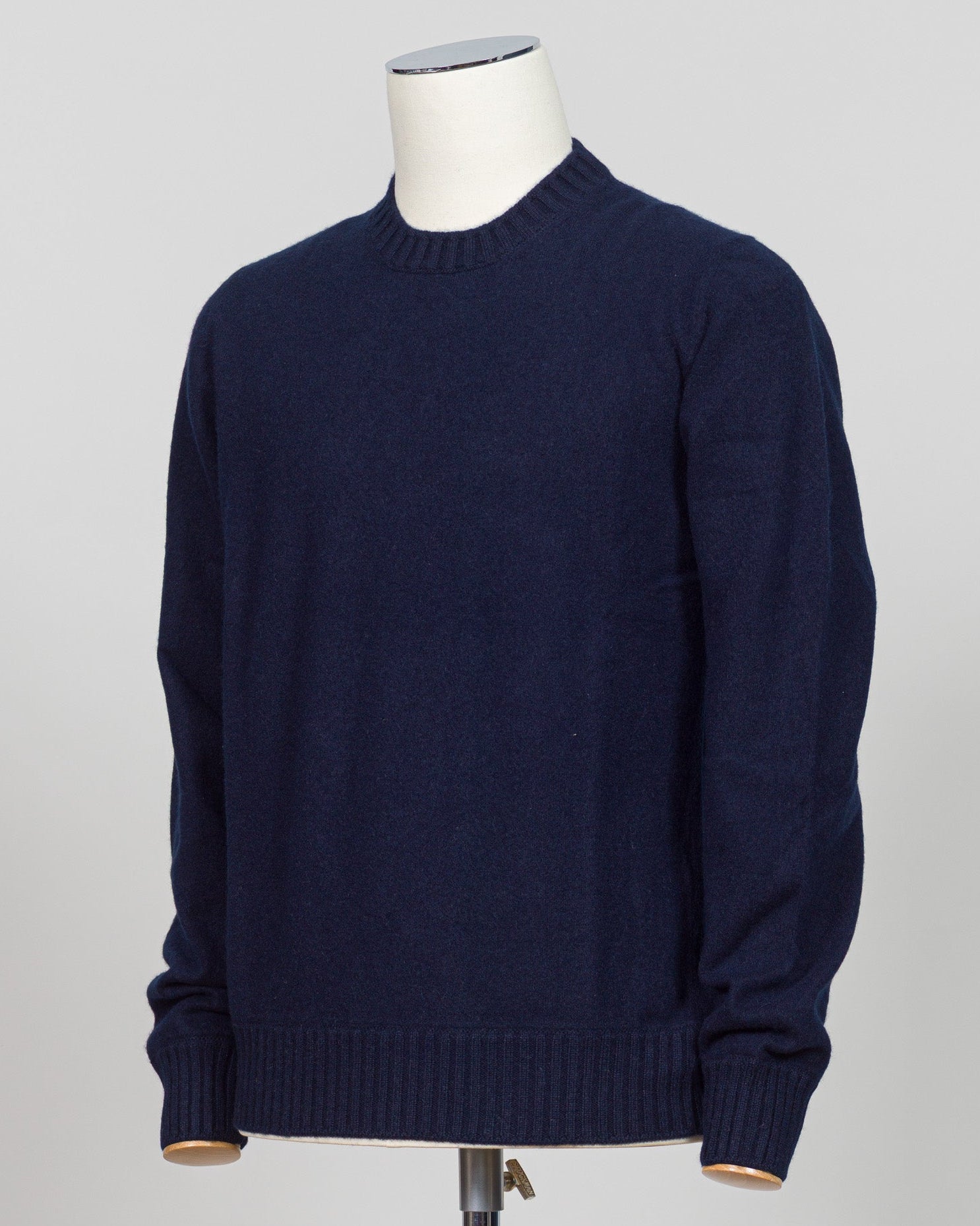 A dark navy blue knit sweater displayed on a white mannequin torso against a light gray studio background. Italian craftsmanship meets luxurious comfort in this Gran Sasso felted cashmere crewneck. The substantial weight and refined texture of premium cashmere deliver warmth without bulk, while the timeless silver tone pairs effortlessly with tailored trousers or structured outerwear.  A foundational piece for the wardrobe—versatile enough for layering, refined enough to stand alone. Gran Sasso Felted Cashm