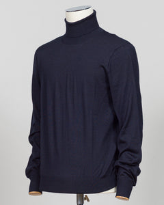 A dark navy blue knit turtleneck sweater displayed on a white mannequin torso against a light gray  Refined luxury knitwear from Gran Sasso, combining wool, cashmere, and silk in a timeless roll neck silhouette. The navy colorway offers versatile sophistication—equally at home layered under tailoring or worn as a standalone piece. Soft, breathable construction ensures comfort across seasons, while the blend of natural fibers delivers lasting durability and subtle sheen.A wardrobe essentia studio background.