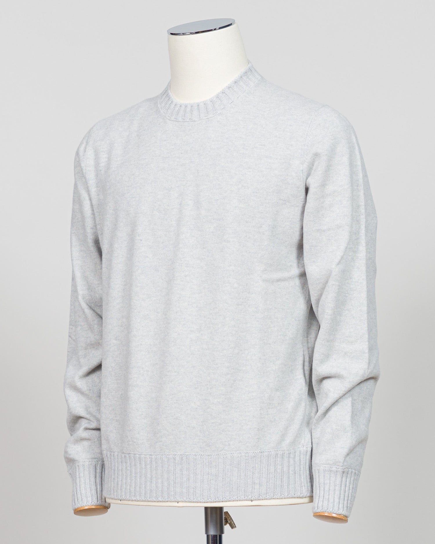 A light gray heather crewneck sweater displayed on a white dress form mannequin against a neutral light gray background. Italian craftsmanship meets luxurious comfort in this Gran Sasso felted cashmere crewneck. The substantial weight and refined texture of premium cashmere deliver warmth without bulk, while the timeless silver tone pairs effortlessly with tailored trousers or structured outerwear. A foundational piece for the discerning wardrobe—versatile enough for layering, refined enough to stand alone.