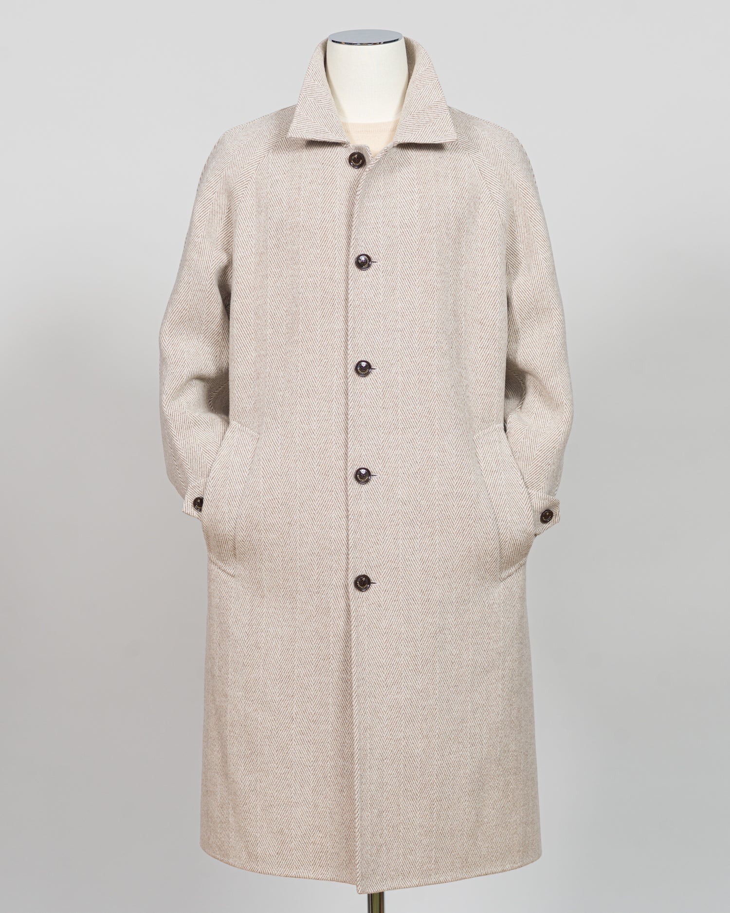 A light beige textured wool-blend coat with a collar, front buttons, and side pockets, displayed on a mannequin against a neutral gray background.