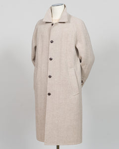 A light beige wool-blend coat displayed on a mannequin against a neutral light gray background. The coat features a classic collar, a front button closure with dark buttons, and large front patch pockets.