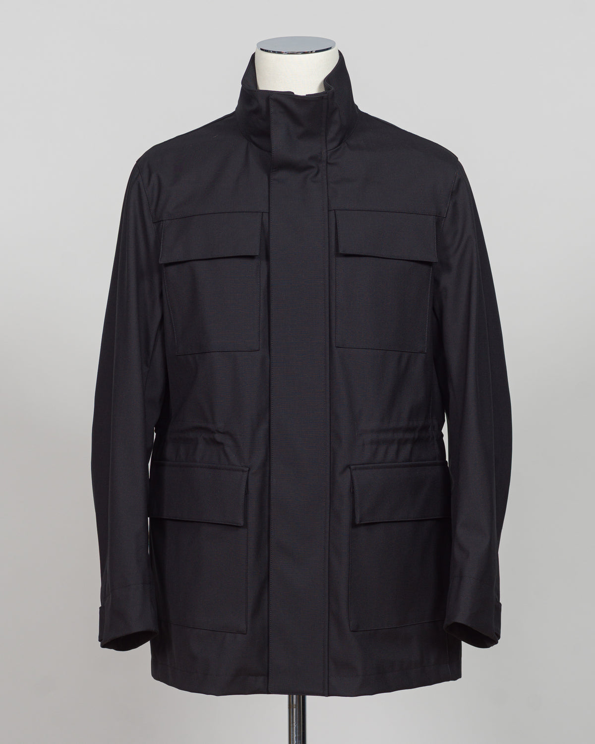 A black utility jacket with a high stand-up collar, displayed on a white mannequin torso against a neutral gray background.