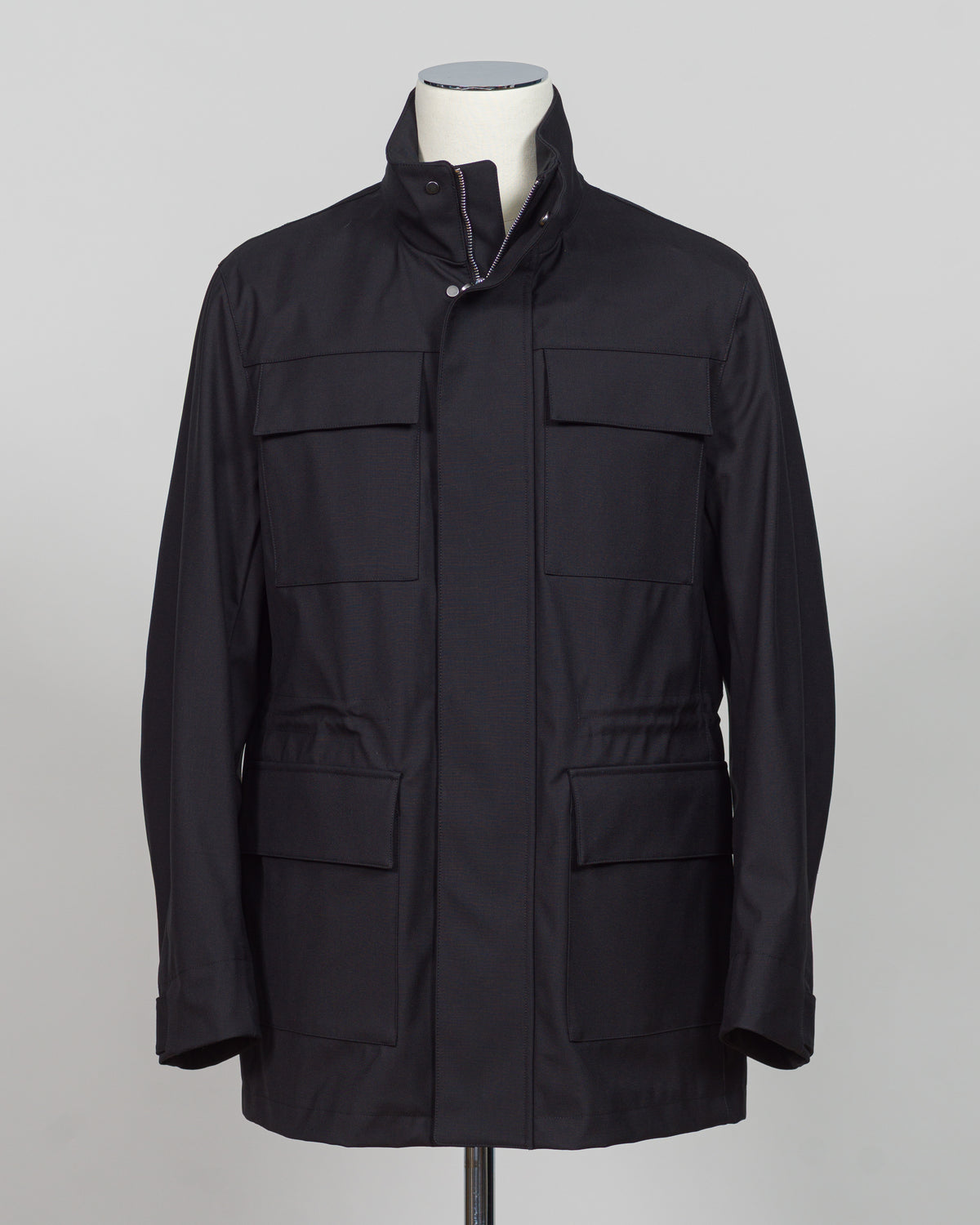 A black utility jacket displayed on a mannequin torso against a light gray studio background. The jacket features a high collar, a front zipper closure, and four large front flap pockets.
