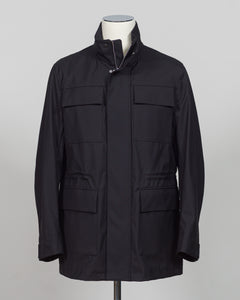 A black utility jacket displayed on a mannequin torso against a light gray studio background. The jacket features a high collar, a front zipper closure, and four large front flap pockets.